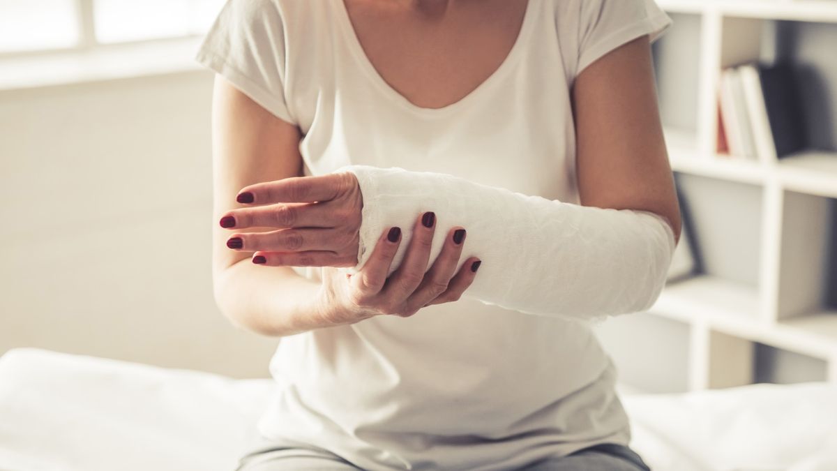 Mid-section of a woman sat down. She has a white medical cast on her left arm which she is supporting with her right hand.